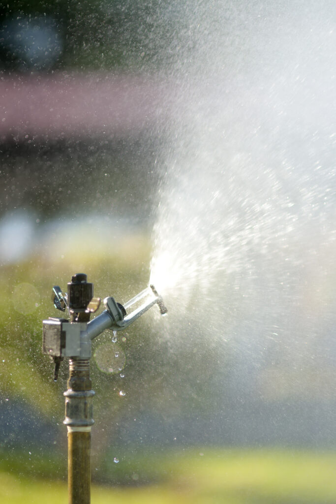 Asperseur métallique projetant de l'eau en plein soleil dans un jardin
